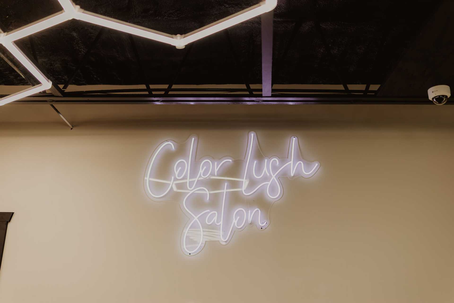 Neon sign reading "Color Lush Salon" on a beige wall.
