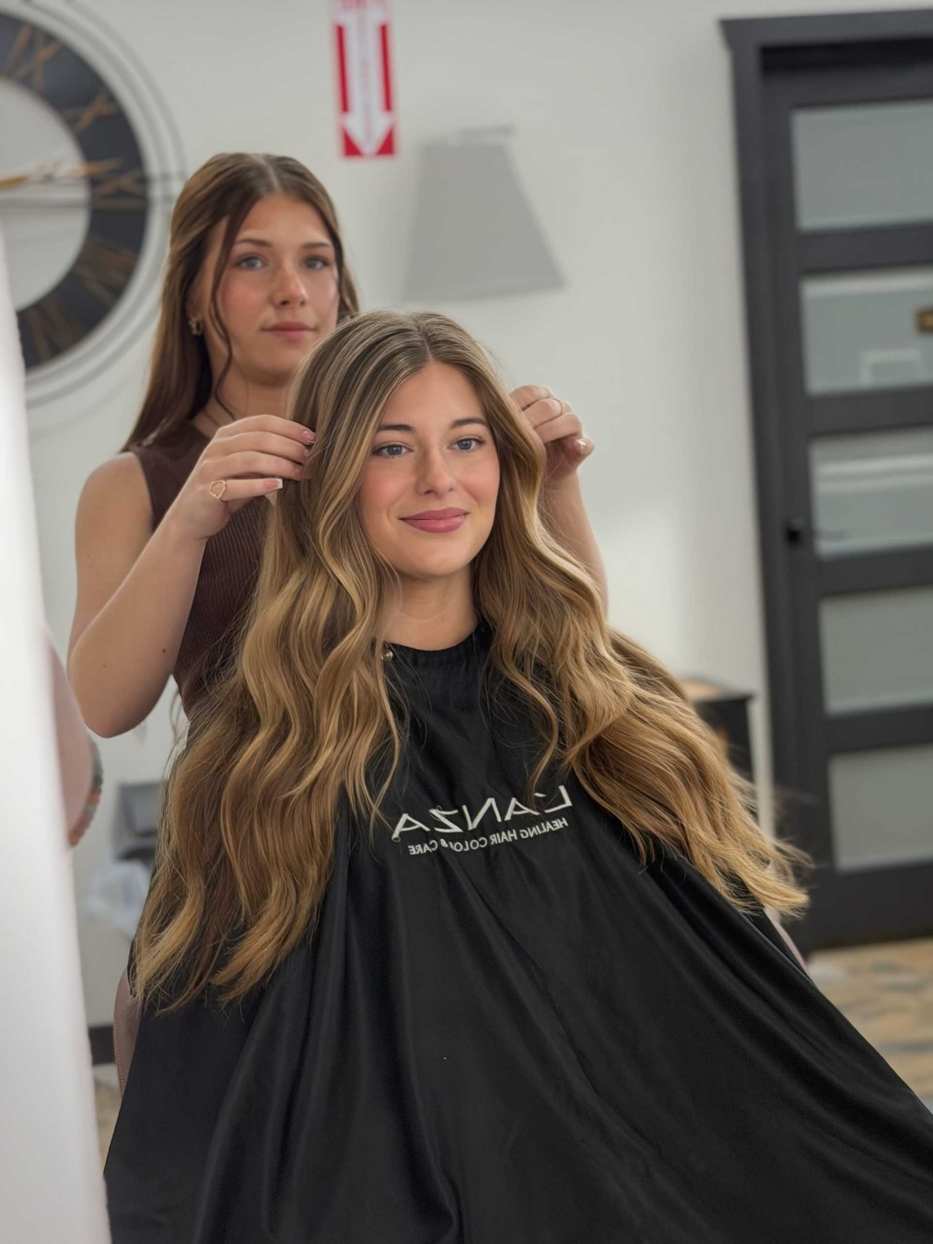 Woman in salon getting her long, wavy hair styled by a hairdresser.